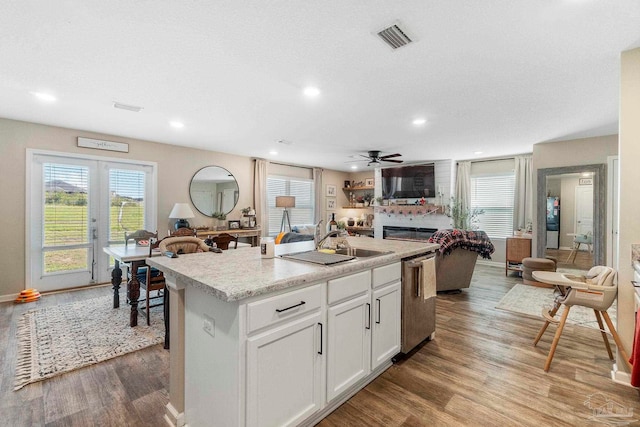 kitchen featuring visible vents, stainless steel dishwasher, a glass covered fireplace, open floor plan, and an island with sink