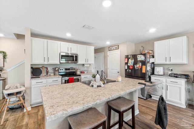 kitchen with hardwood / wood-style flooring, appliances with stainless steel finishes, and an island with sink