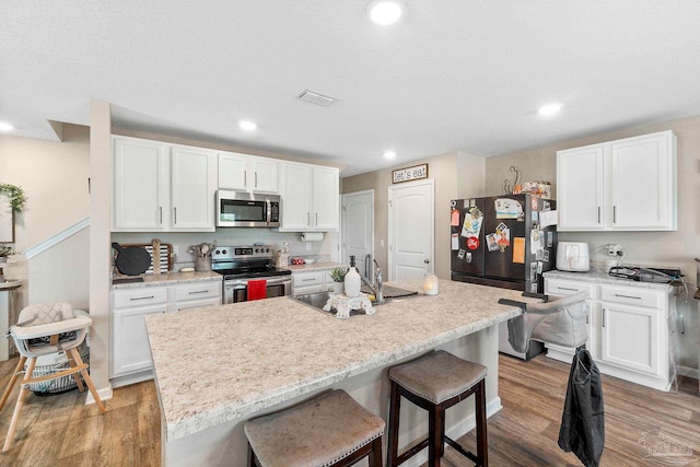 kitchen featuring a breakfast bar area, stainless steel appliances, wood finished floors, a sink, and white cabinetry