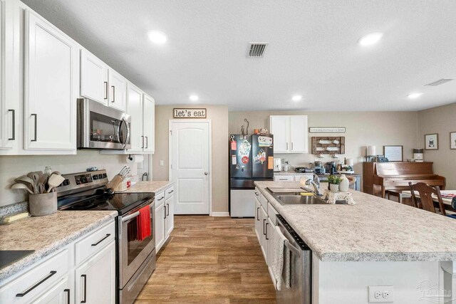 kitchen featuring stainless steel appliances, a center island with sink, white cabinets, a textured ceiling, and light wood-type flooring