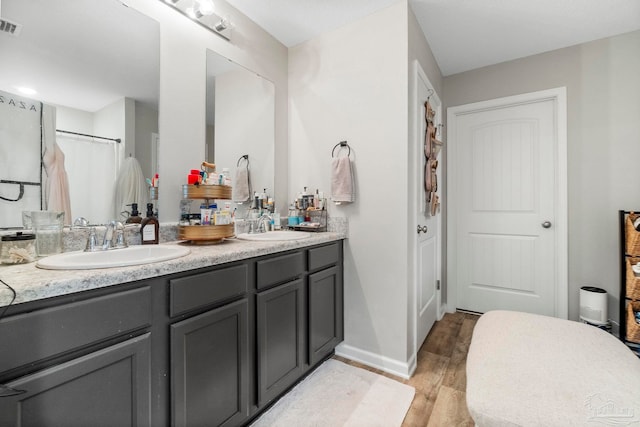 full bathroom with double vanity, visible vents, a sink, and wood finished floors