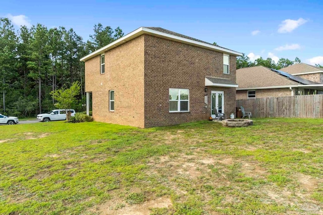 back of property with a fire pit, fence, a lawn, and brick siding