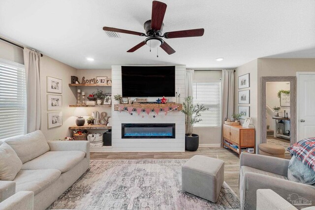 living room with a large fireplace, light hardwood / wood-style flooring, a wealth of natural light, and ceiling fan