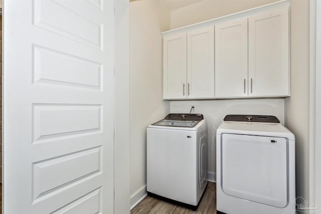 clothes washing area featuring washing machine and clothes dryer, wood-type flooring, and cabinets