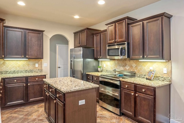 kitchen featuring light stone counters, stainless steel appliances, tasteful backsplash, and a center island