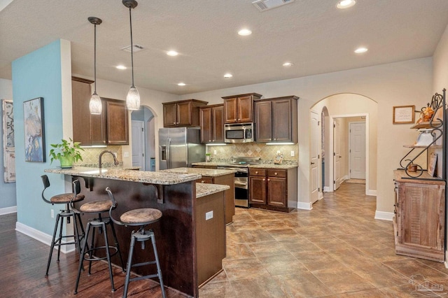 kitchen with kitchen peninsula, tasteful backsplash, hanging light fixtures, light stone countertops, and stainless steel appliances