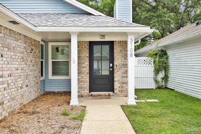 3108 Station Ct, Pensacola, FL 32504 - view of exterior entry featuring a shingled roof, a chimney, a lawn, and covered porch