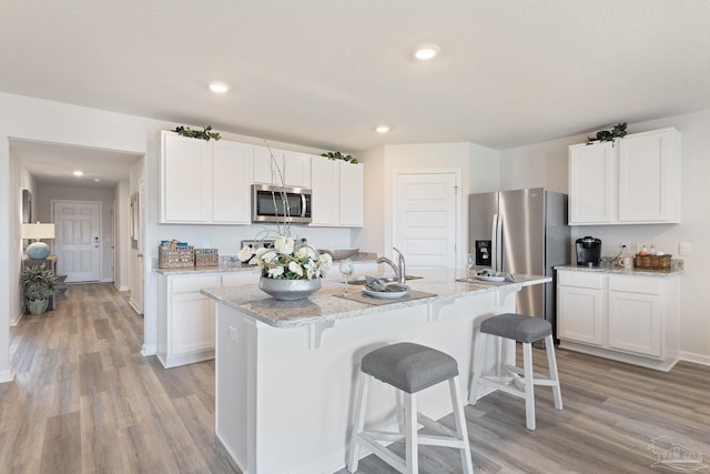 kitchen with a kitchen breakfast bar, light wood finished floors, white cabinets, and stainless steel appliances