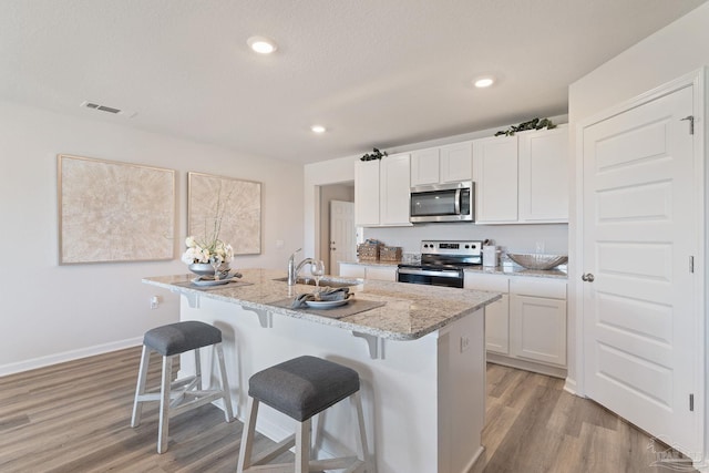 kitchen with visible vents, a sink, appliances with stainless steel finishes, a kitchen breakfast bar, and a kitchen island with sink