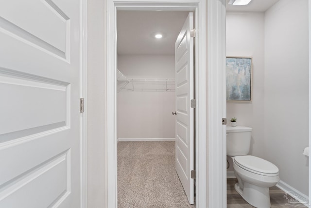 bathroom featuring a walk in closet, baseboards, and toilet