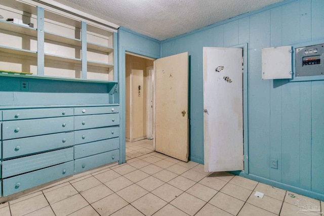 interior space featuring light tile patterned flooring, wood walls, and a textured ceiling