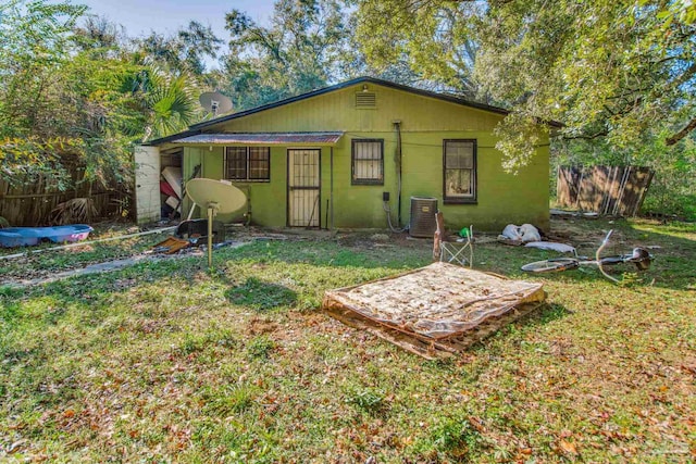 rear view of house featuring central air condition unit, a lawn, concrete block siding, and fence