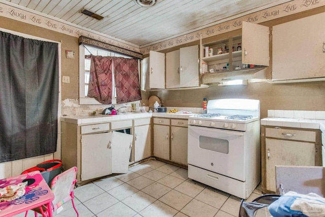 kitchen with tile countertops, white range with gas cooktop, light tile patterned flooring, a sink, and wooden ceiling