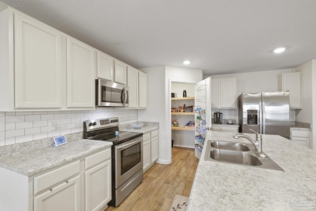 kitchen with sink, white cabinetry, light wood-type flooring, decorative backsplash, and appliances with stainless steel finishes