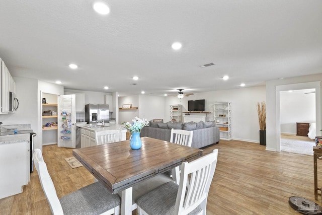 dining area featuring light wood-type flooring, ceiling fan, a textured ceiling, a fireplace, and sink