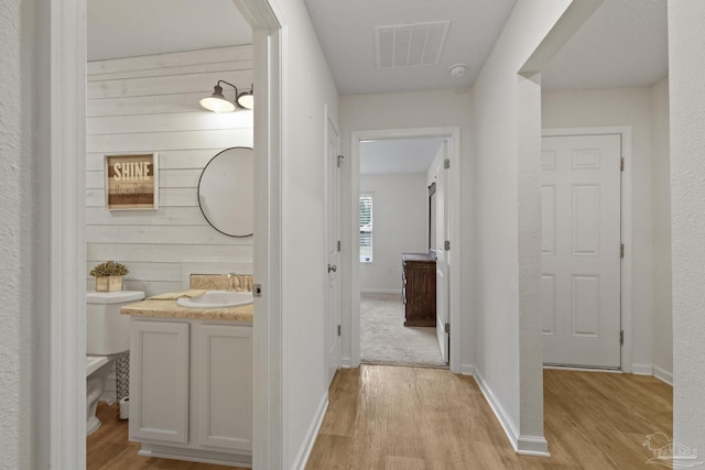 hallway featuring sink, wooden walls, and light hardwood / wood-style floors