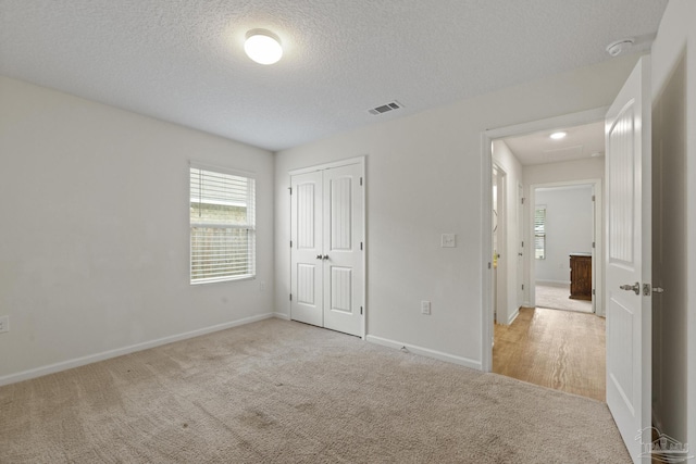 unfurnished bedroom featuring a textured ceiling, light colored carpet, and a closet