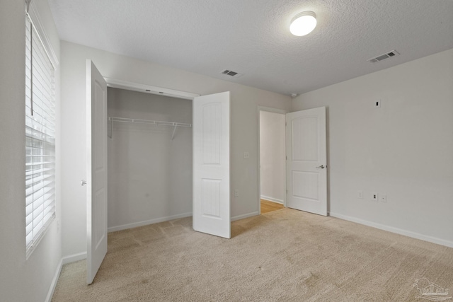 unfurnished bedroom featuring a textured ceiling, light colored carpet, a closet, and multiple windows