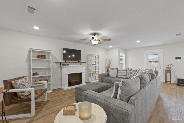 living room with light hardwood / wood-style floors, ceiling fan, and a textured ceiling