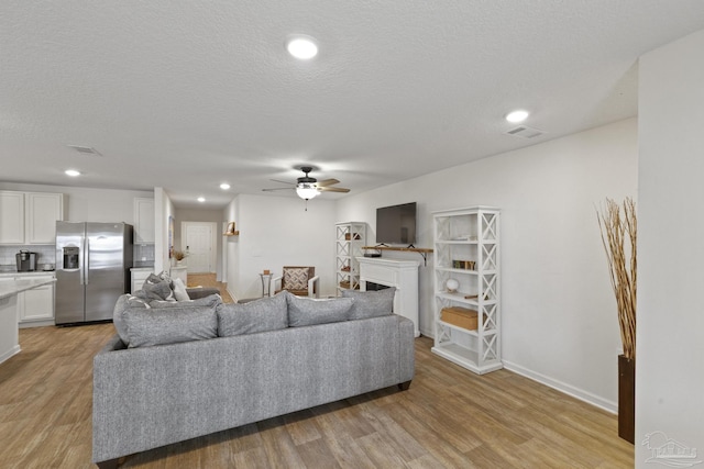 living room featuring light wood-type flooring, ceiling fan, and a textured ceiling