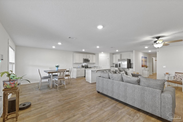 living room with a textured ceiling, ceiling fan, and light hardwood / wood-style flooring