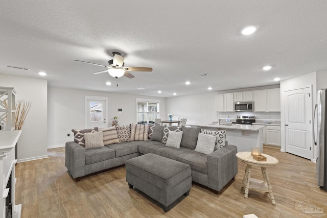 living room featuring sink, ceiling fan, light wood-type flooring, and a textured ceiling