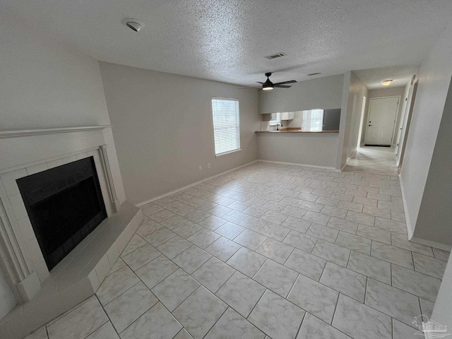 unfurnished living room featuring baseboards, visible vents, a fireplace, ceiling fan, and a textured ceiling