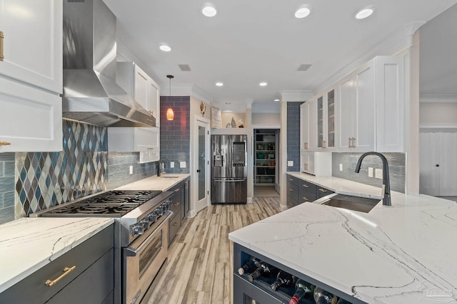 kitchen with stainless steel appliances, wall chimney range hood, a sink, and white cabinetry