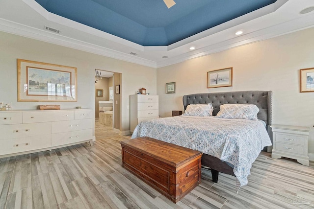 bedroom featuring light wood-style floors, connected bathroom, visible vents, and a tray ceiling