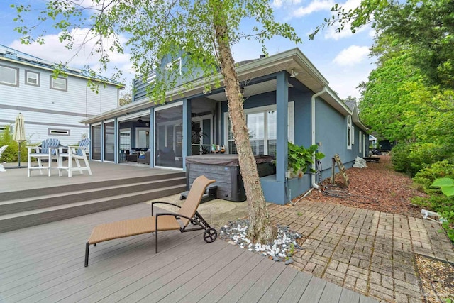 back of property with a sunroom, a hot tub, a deck, and stucco siding