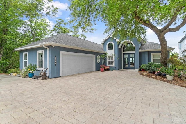 ranch-style house featuring a garage, roof with shingles, decorative driveway, french doors, and stucco siding