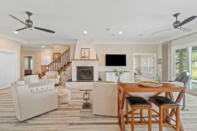 living room with ceiling fan, visible vents, crown molding, and a stone fireplace