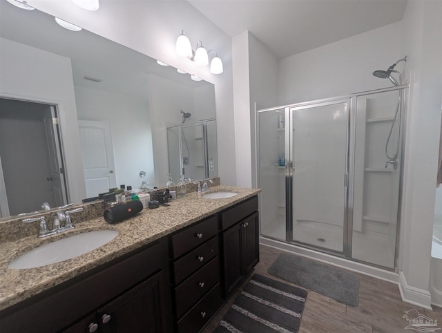 full bath with double vanity, a shower stall, a sink, and wood finished floors