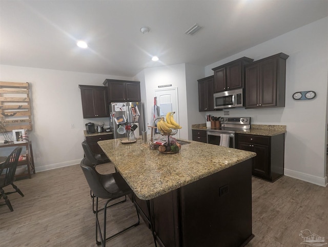 kitchen with appliances with stainless steel finishes, wood finished floors, visible vents, and light stone countertops