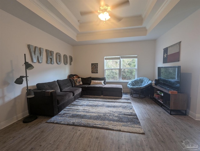 living room featuring ornamental molding, a tray ceiling, wood finished floors, and baseboards