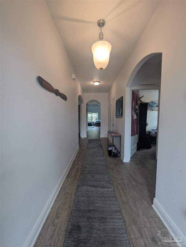 hallway with arched walkways, dark wood-type flooring, and baseboards