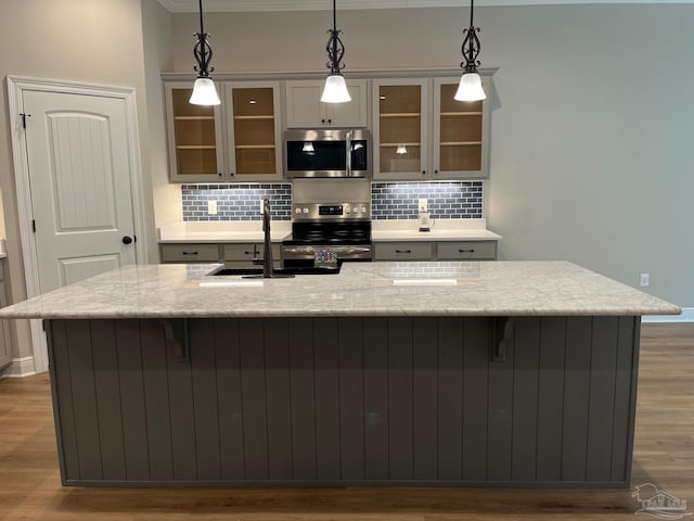 kitchen featuring hanging light fixtures, decorative backsplash, light stone countertops, light wood-type flooring, and appliances with stainless steel finishes