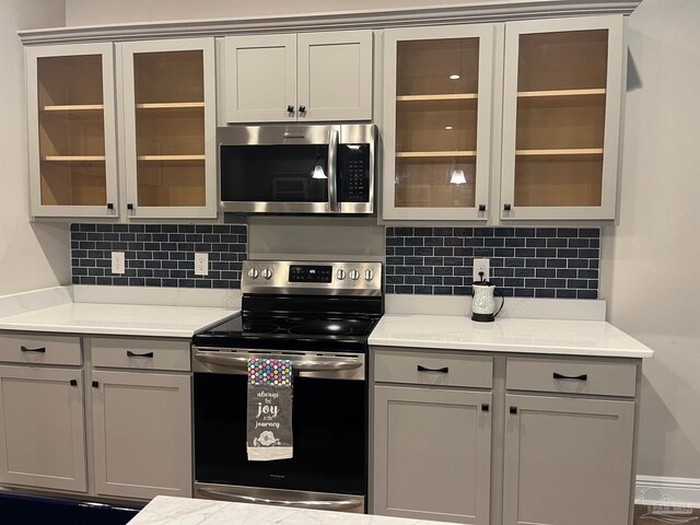 kitchen featuring decorative backsplash, stainless steel appliances, crown molding, pendant lighting, and gray cabinets