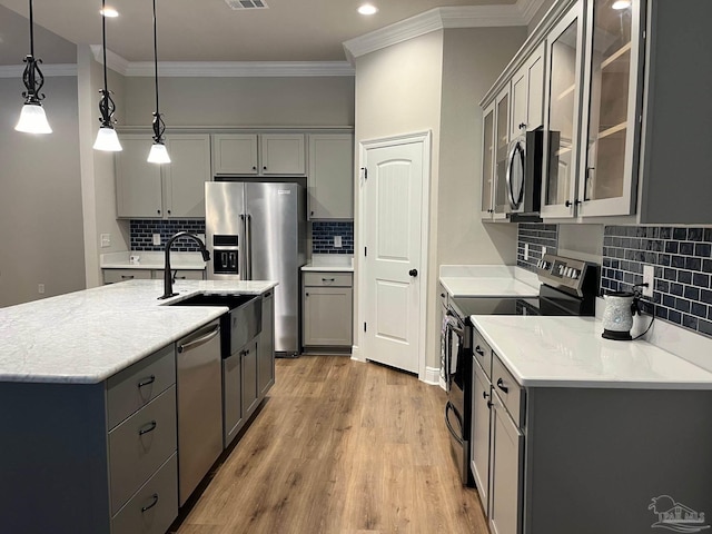 kitchen with pendant lighting, backsplash, appliances with stainless steel finishes, and light hardwood / wood-style flooring