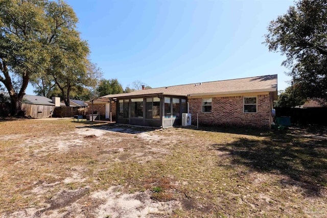 rear view of property featuring a yard, a sunroom, brick siding, and fence