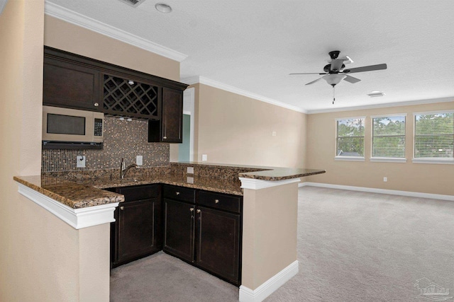 kitchen featuring dark stone countertops, light carpet, kitchen peninsula, ceiling fan, and tasteful backsplash