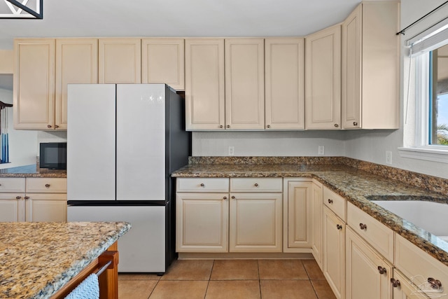 2950 Coral Strip Pkwy, Gulf Breeze, FL 32563 - kitchen featuring freestanding refrigerator, cream cabinets, black microwave, light tile patterned flooring, and dark stone countertops