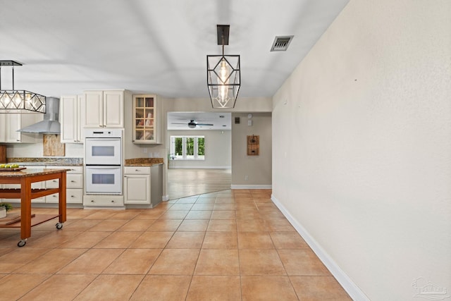 2950 Coral Strip Pkwy, Gulf Breeze, FL 32563 - kitchen featuring wall chimney range hood, white double oven, glass insert cabinets, light tile patterned flooring, and decorative light fixtures