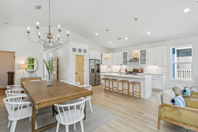 dining room with sink, a notable chandelier, high vaulted ceiling, and light hardwood / wood-style flooring