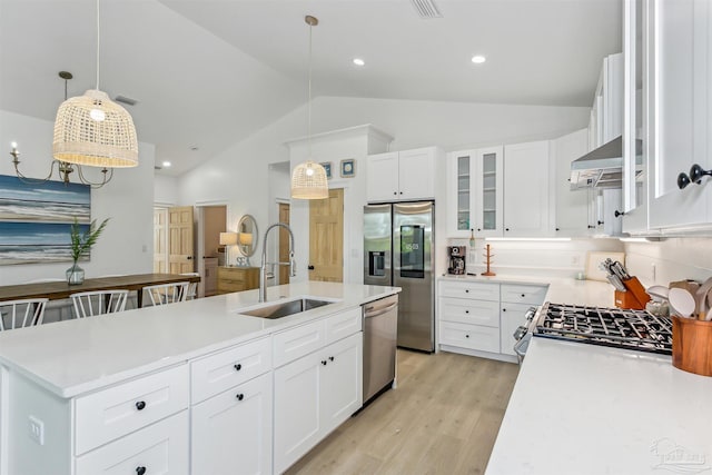 kitchen with sink, white cabinets, hanging light fixtures, stainless steel appliances, and wall chimney range hood