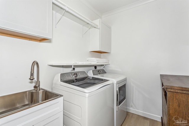 clothes washing area featuring cabinets, washing machine and dryer, sink, and light hardwood / wood-style floors