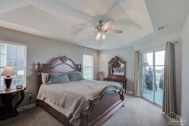 carpeted bedroom featuring access to exterior, a textured ceiling, a tray ceiling, and ceiling fan