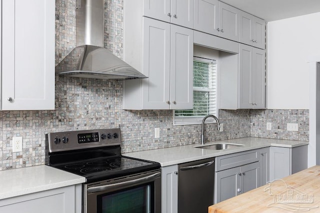 kitchen with wall chimney range hood, appliances with stainless steel finishes, sink, backsplash, and butcher block counters