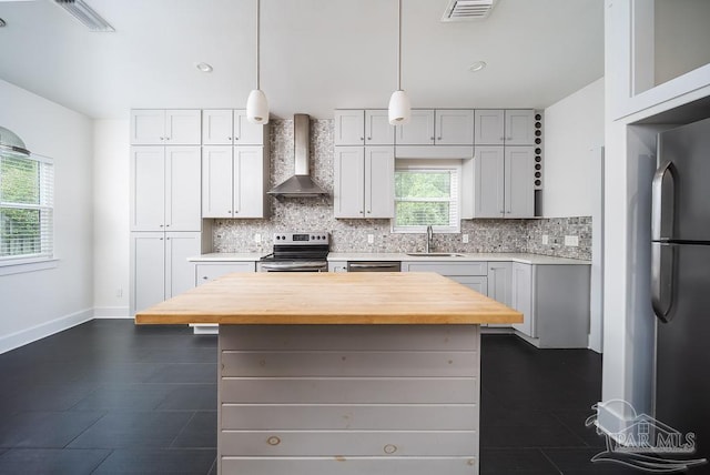 kitchen featuring a kitchen island, wall chimney range hood, sink, pendant lighting, and appliances with stainless steel finishes