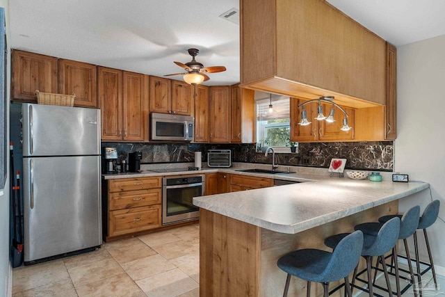 kitchen featuring appliances with stainless steel finishes, sink, decorative backsplash, hanging light fixtures, and kitchen peninsula